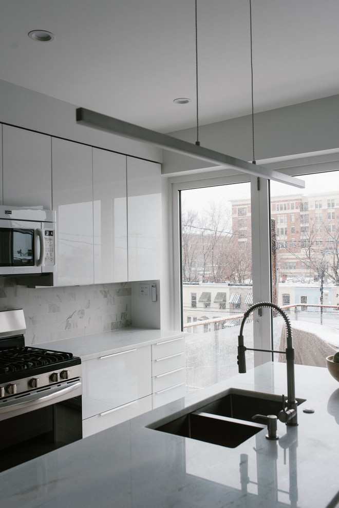 Example of a small minimalist single-wall light wood floor and beige floor eat-in kitchen design in Baltimore with a double-bowl sink, flat-panel cabinets, white cabinets, marble countertops, white backsplash, marble backsplash, stainless steel appliances, an island and white countertops
