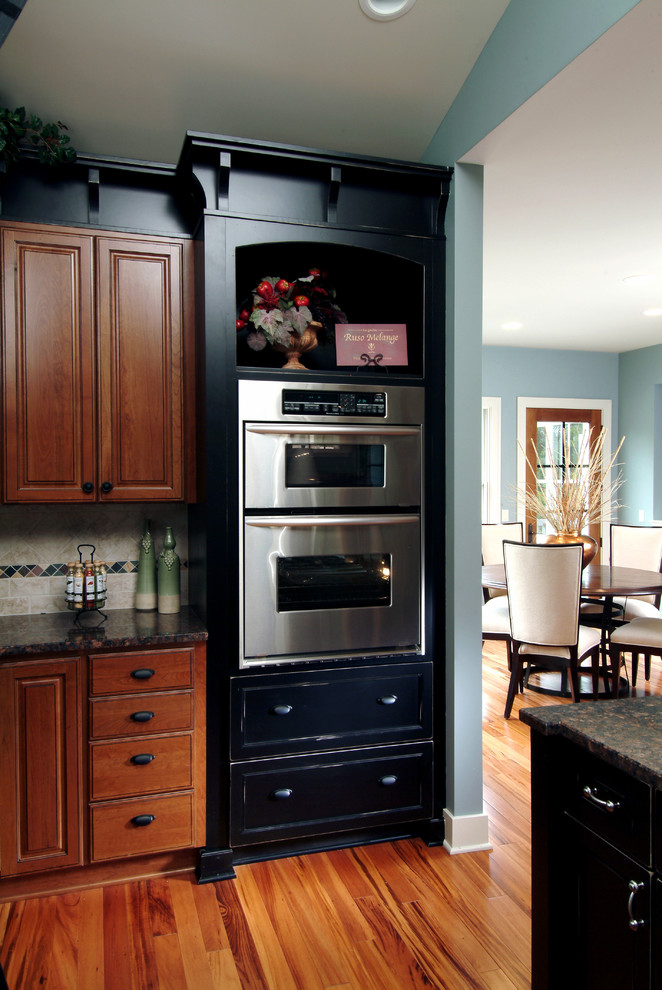 Exempel på ett mellanstort klassiskt linjärt kök och matrum, med en dubbel diskho, luckor med infälld panel, skåp i mörkt trä, granitbänkskiva, grått stänkskydd, stänkskydd i stenkakel, rostfria vitvaror, mellanmörkt trägolv och en köksö