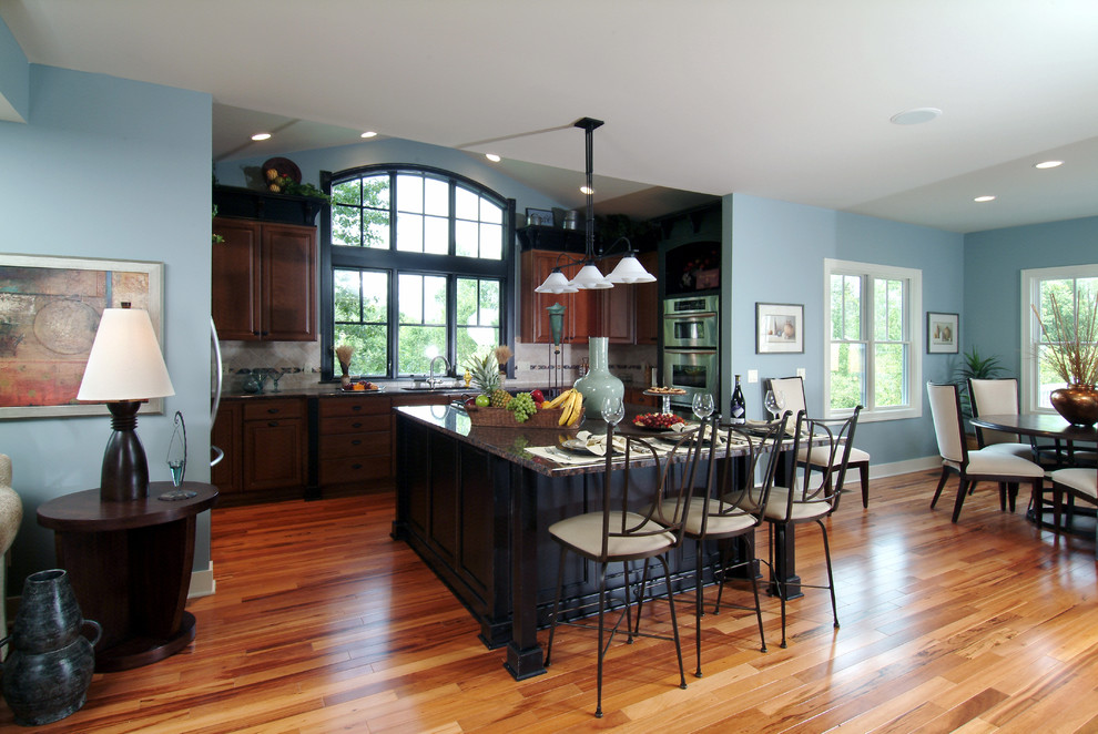 Bild på ett mellanstort vintage linjärt kök och matrum, med luckor med infälld panel, skåp i mörkt trä, granitbänkskiva, grått stänkskydd, stänkskydd i stenkakel, rostfria vitvaror, mellanmörkt trägolv, en köksö och en dubbel diskho