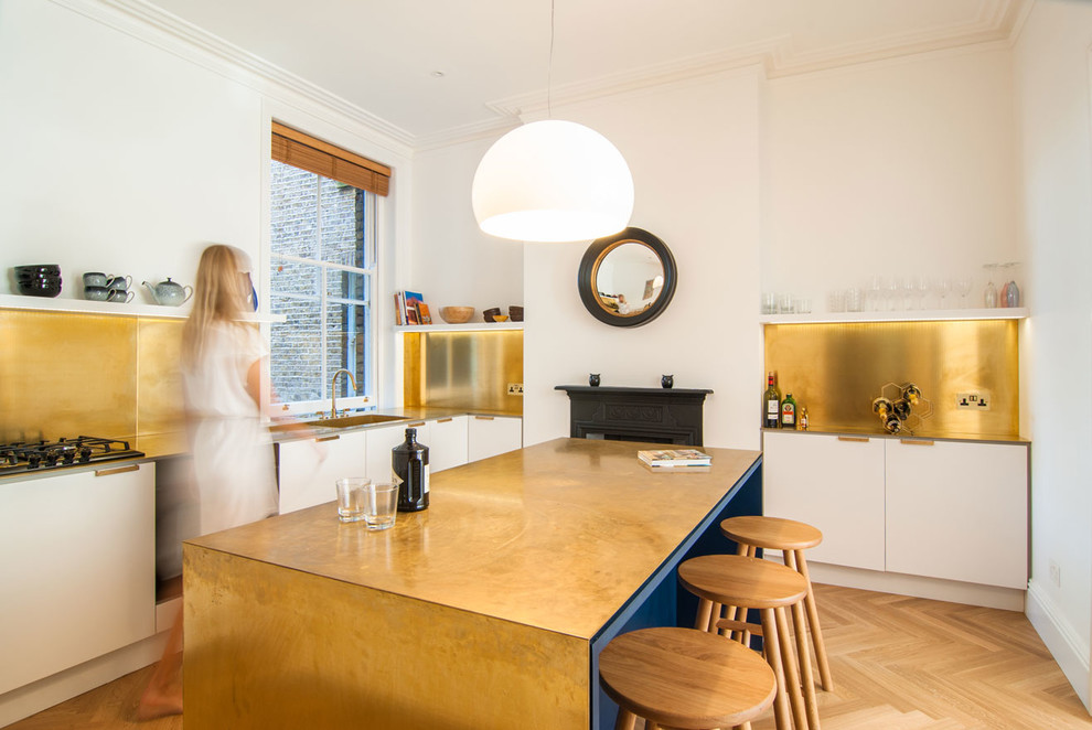 Immagine di un cucina con isola centrale contemporaneo di medie dimensioni con ante lisce, ante bianche, lavello a vasca singola, paraspruzzi a effetto metallico, parquet chiaro e pavimento beige