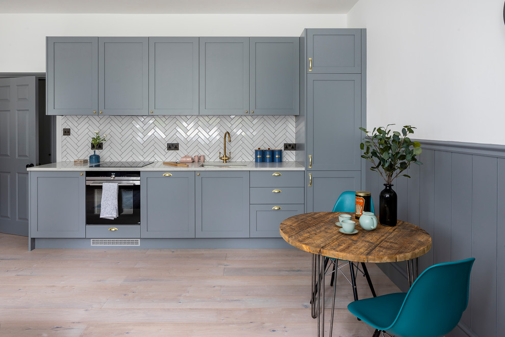 Example of a small trendy single-wall medium tone wood floor and beige floor eat-in kitchen design in Hertfordshire with an undermount sink, shaker cabinets, gray cabinets, quartzite countertops, white backsplash, black appliances, no island and white countertops