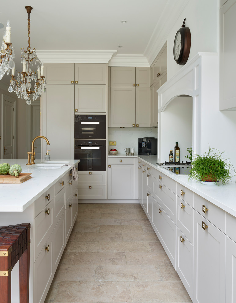 Klassisk inredning av ett mellanstort vit vitt l-kök, med en undermonterad diskho, luckor med infälld panel, grå skåp, bänkskiva i kvartsit, en köksö och beiget golv