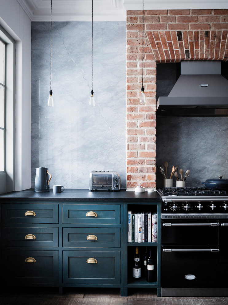 This is an example of a medium sized traditional single-wall kitchen in London with recessed-panel cabinets, blue cabinets, black appliances, black worktops, grey splashback and dark hardwood flooring.