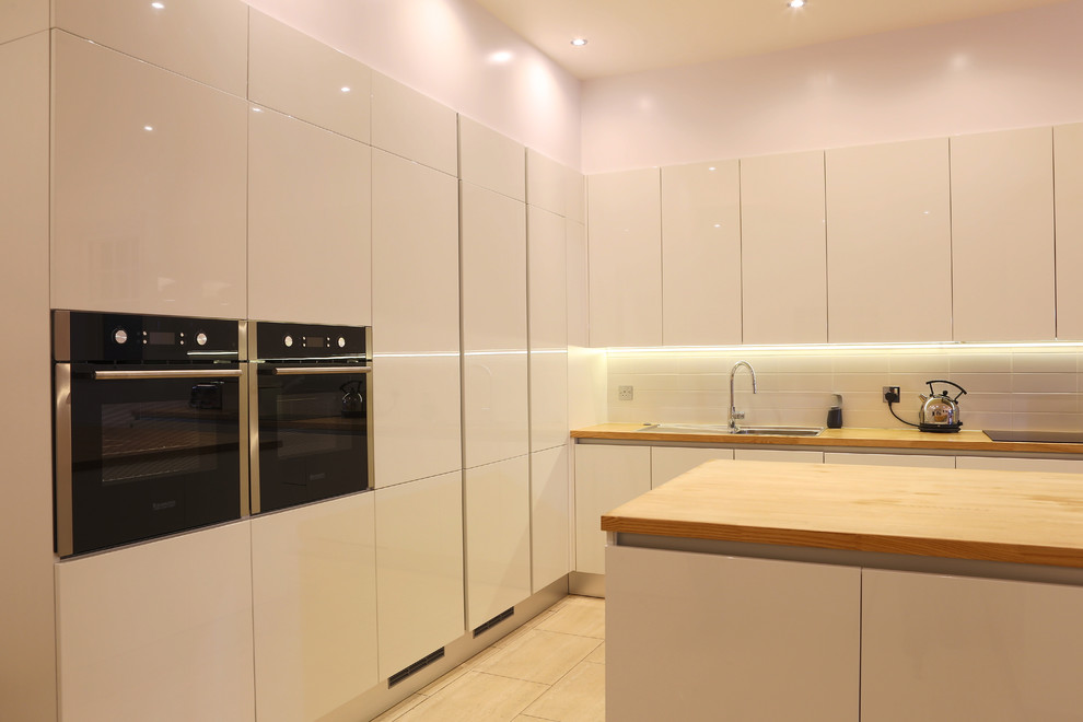 Medium sized contemporary l-shaped kitchen/diner in London with a single-bowl sink, wood worktops, ceramic splashback, stainless steel appliances, ceramic flooring and an island.