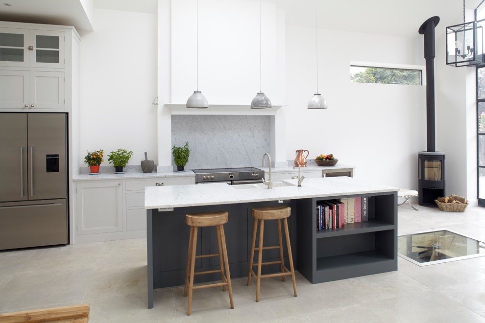 Photo of a medium sized contemporary galley kitchen in London with a belfast sink, shaker cabinets, grey cabinets, marble worktops, marble splashback, stainless steel appliances, porcelain flooring, an island, white splashback, grey floors and grey worktops.