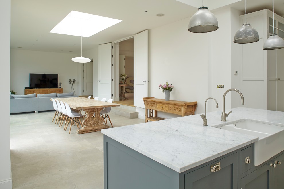 Medium sized traditional open plan kitchen in London with a belfast sink, shaker cabinets, grey cabinets, marble worktops, marble splashback, stainless steel appliances, porcelain flooring and an island.