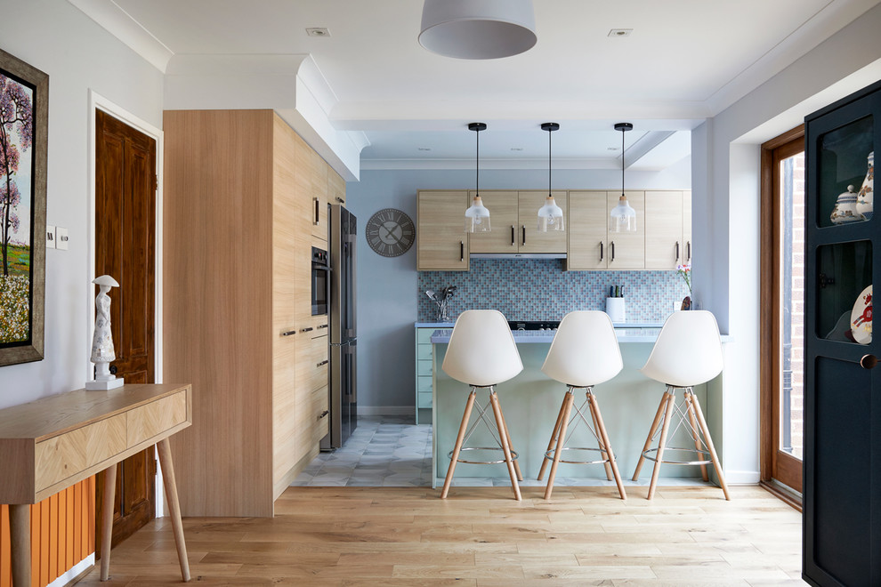 Klassische Wohnküche in L-Form mit bunter Rückwand, blauer Arbeitsplatte, flächenbündigen Schrankfronten, grünen Schränken, Rückwand aus Mosaikfliesen, Küchengeräten aus Edelstahl, Halbinsel und grauem Boden in London