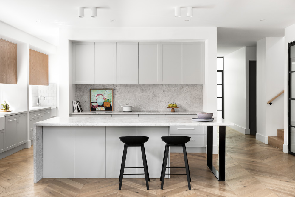 Moderne Küche in L-Form mit Landhausspüle, Schrankfronten im Shaker-Stil, grauen Schränken, Küchenrückwand in Grau, Rückwand aus Stein, braunem Holzboden, Kücheninsel, braunem Boden und grauer Arbeitsplatte in Melbourne