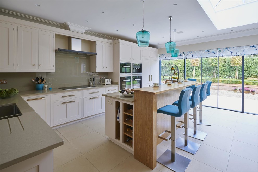 This is an example of a medium sized classic l-shaped kitchen in Surrey with shaker cabinets, quartz worktops, an island, beige cabinets, grey splashback, glass sheet splashback, black appliances, beige floors and grey worktops.