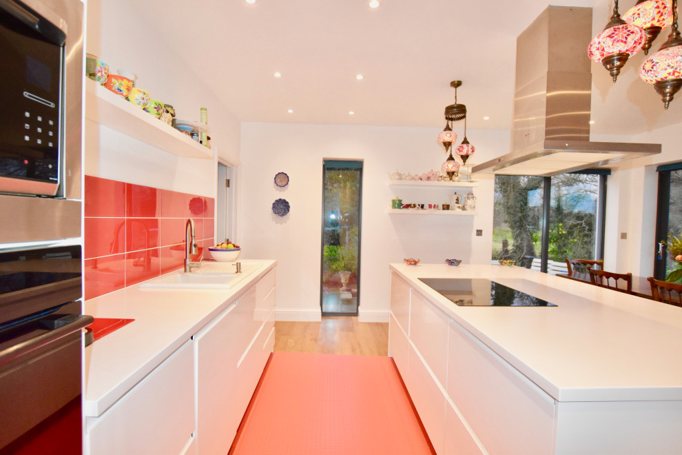 サリーにあるモダンスタイルのおしゃれなキッチン (白いキャビネット、赤いキッチンパネル、セラミックタイルのキッチンパネル、パネルと同色の調理設備、無垢フローリング、茶色い床、白いキッチンカウンター) の写真