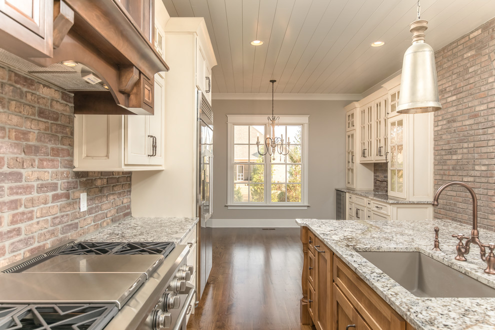 Exempel på ett mellanstort amerikanskt linjärt kök och matrum, med en undermonterad diskho, luckor med infälld panel, vita skåp, granitbänkskiva, rött stänkskydd, stänkskydd i tegel, rostfria vitvaror, mörkt trägolv och en köksö