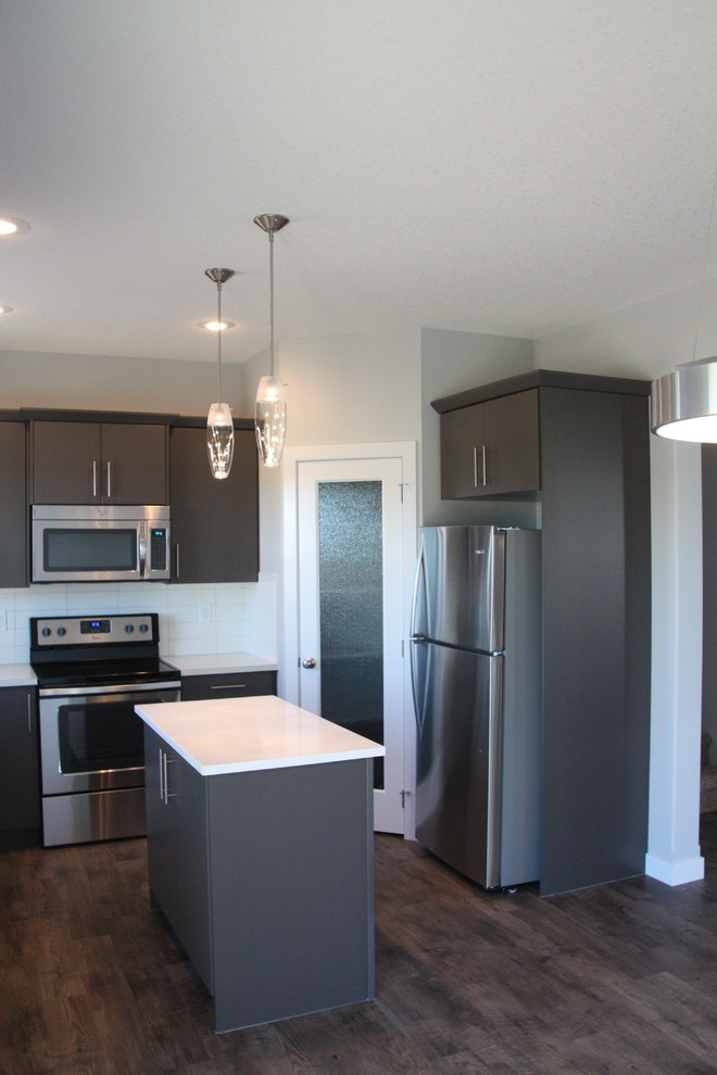 Small traditional u-shaped kitchen/diner in Calgary with a double-bowl sink, flat-panel cabinets, grey cabinets, laminate countertops, white splashback, ceramic splashback, stainless steel appliances, lino flooring and an island.
