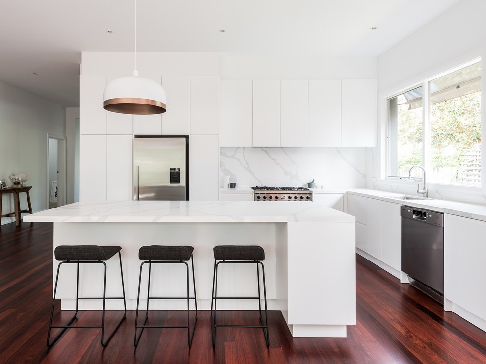 Open concept kitchen - mid-sized modern single-wall dark wood floor and brown floor open concept kitchen idea in Melbourne with a drop-in sink, flat-panel cabinets, white cabinets, white backsplash, ceramic backsplash, stainless steel appliances, an island and white countertops