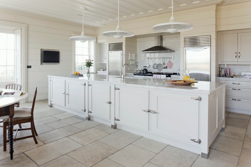 Cette photo montre une cuisine américaine chic avec un évier encastré, des portes de placard blanches, une crédence blanche, une crédence en dalle de pierre et un électroménager en acier inoxydable.