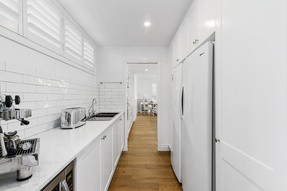 Design ideas for a large classic galley kitchen pantry in Gold Coast - Tweed with a submerged sink, shaker cabinets, white cabinets, engineered stone countertops, white splashback, metro tiled splashback, stainless steel appliances, lino flooring, an island, brown floors and yellow worktops.