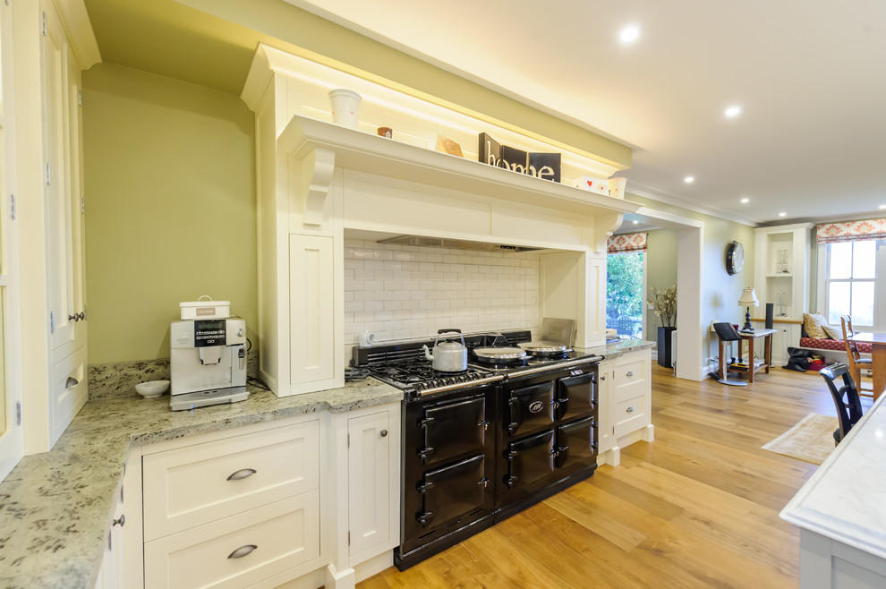 Example of a classic u-shaped kitchen pantry design in Melbourne with a farmhouse sink, recessed-panel cabinets, white cabinets, granite countertops, white backsplash and an island