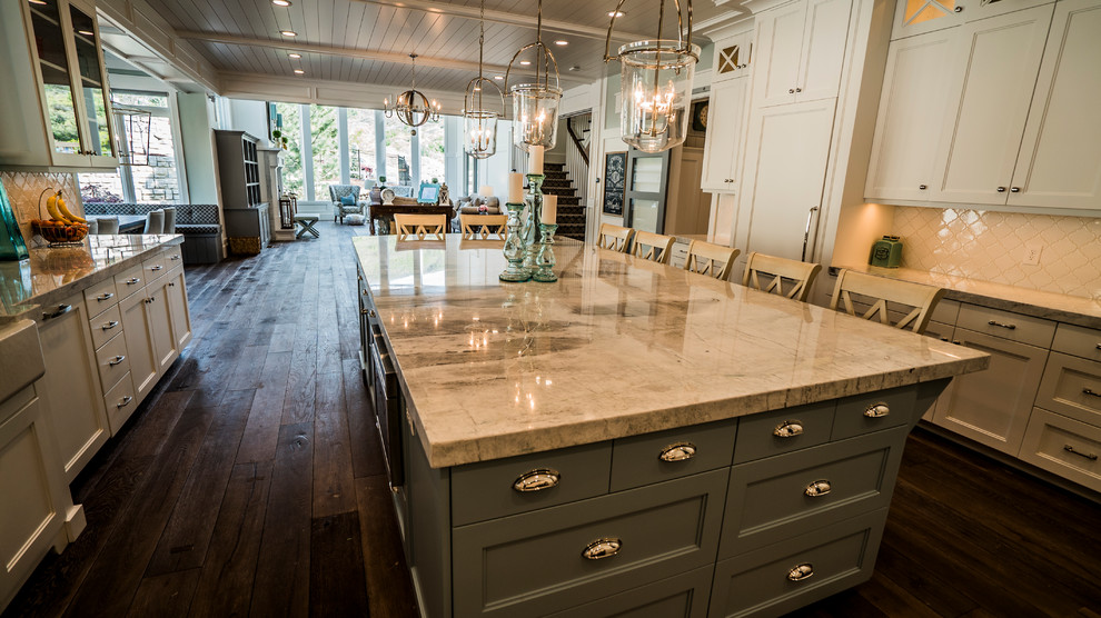 Photo of a large beach style u-shaped open plan kitchen in Salt Lake City with a belfast sink, shaker cabinets, white cabinets, marble worktops, white splashback, stainless steel appliances, dark hardwood flooring, an island and brown floors.