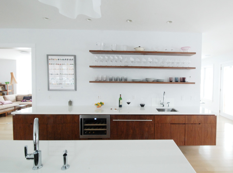 Modern inredning av ett kök och matrum, med en undermonterad diskho, skåp i mörkt trä, vitt stänkskydd och rostfria vitvaror
