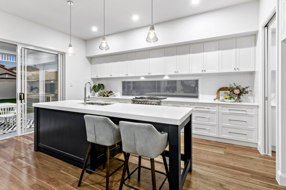 Large galley light wood floor and brown floor kitchen pantry photo in Brisbane with an undermount sink, shaker cabinets, white cabinets, quartz countertops, white backsplash, subway tile backsplash, stainless steel appliances, an island and white countertops