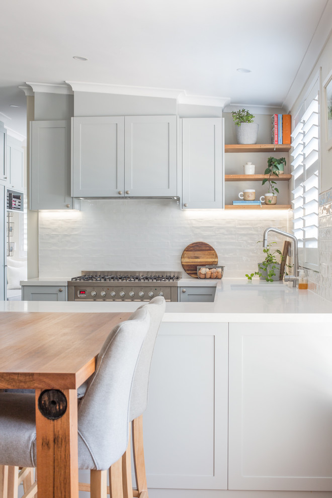 Foto på ett mellanstort funkis vit kök, med en undermonterad diskho, luckor med infälld panel, grå skåp, bänkskiva i kvarts, vitt stänkskydd, stänkskydd i tunnelbanekakel, rostfria vitvaror, klinkergolv i porslin, en halv köksö och grått golv
