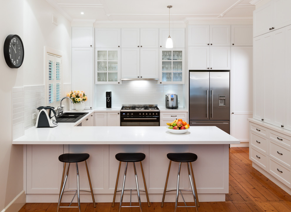 Klassische Küche mit weißen Schränken, Küchenrückwand in Weiß, Rückwand aus Metrofliesen, braunem Holzboden und Halbinsel in Melbourne