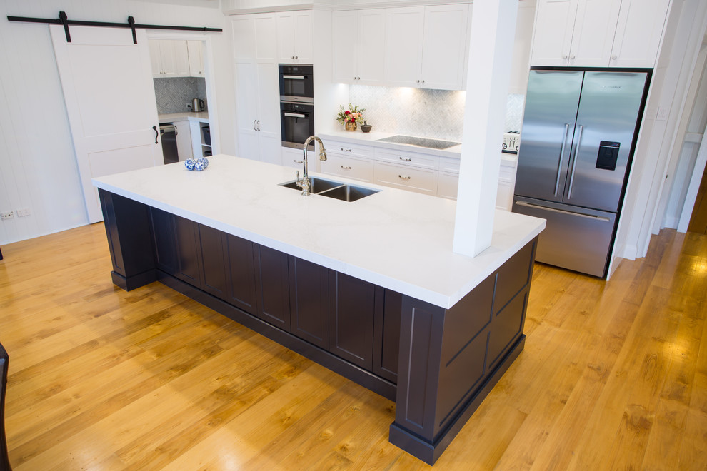Inredning av ett modernt mycket stort vit vitt kök, med en dubbel diskho, skåp i shakerstil, svarta skåp, bänkskiva i kvarts, grått stänkskydd, stänkskydd i marmor, rostfria vitvaror, mellanmörkt trägolv, en köksö och brunt golv