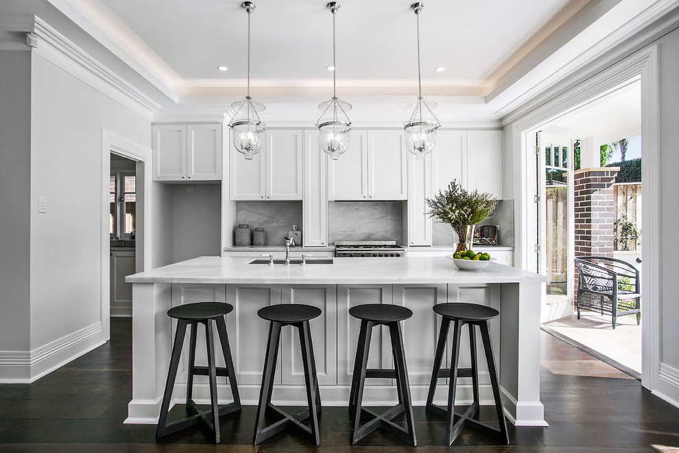 Inspiration for a mid-sized transitional galley dark wood floor and black floor open concept kitchen remodel in Sydney with a farmhouse sink, shaker cabinets, white cabinets, marble countertops, white backsplash, marble backsplash, stainless steel appliances, two islands and white countertops
