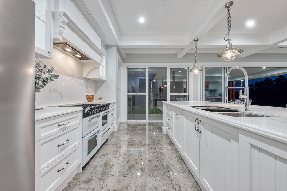 Design ideas for a medium sized farmhouse galley open plan kitchen in Sunshine Coast with a submerged sink, shaker cabinets, white cabinets, engineered stone countertops, white splashback, stone slab splashback, white appliances, marble flooring, an island, grey floors and white worktops.