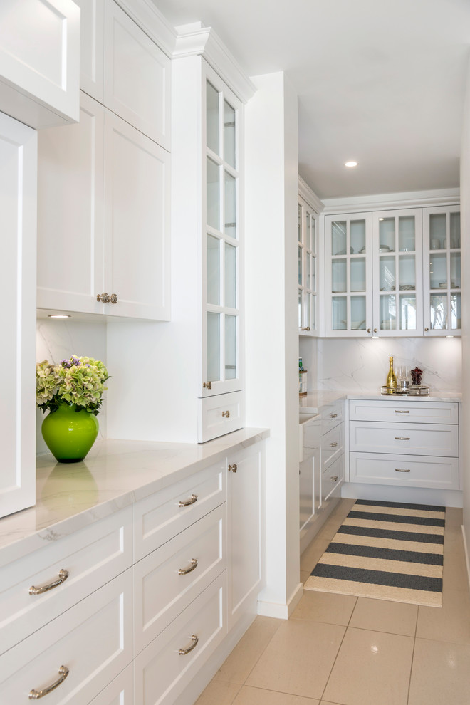 Large nautical galley kitchen/diner in Gold Coast - Tweed with a belfast sink, shaker cabinets, white cabinets, marble worktops, white splashback, marble splashback, stainless steel appliances, ceramic flooring, an island, beige floors and white worktops.