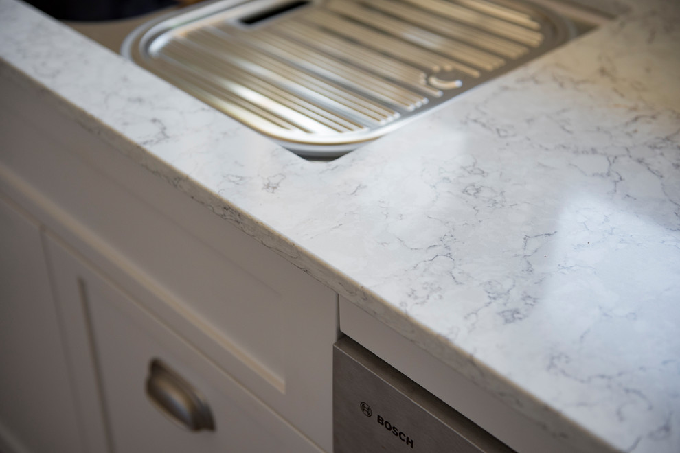 Foto på ett litet maritimt l-kök, med en undermonterad diskho, skåp i shakerstil, vita skåp, bänkskiva i kvarts, vitt stänkskydd, stänkskydd i porslinskakel och rostfria vitvaror