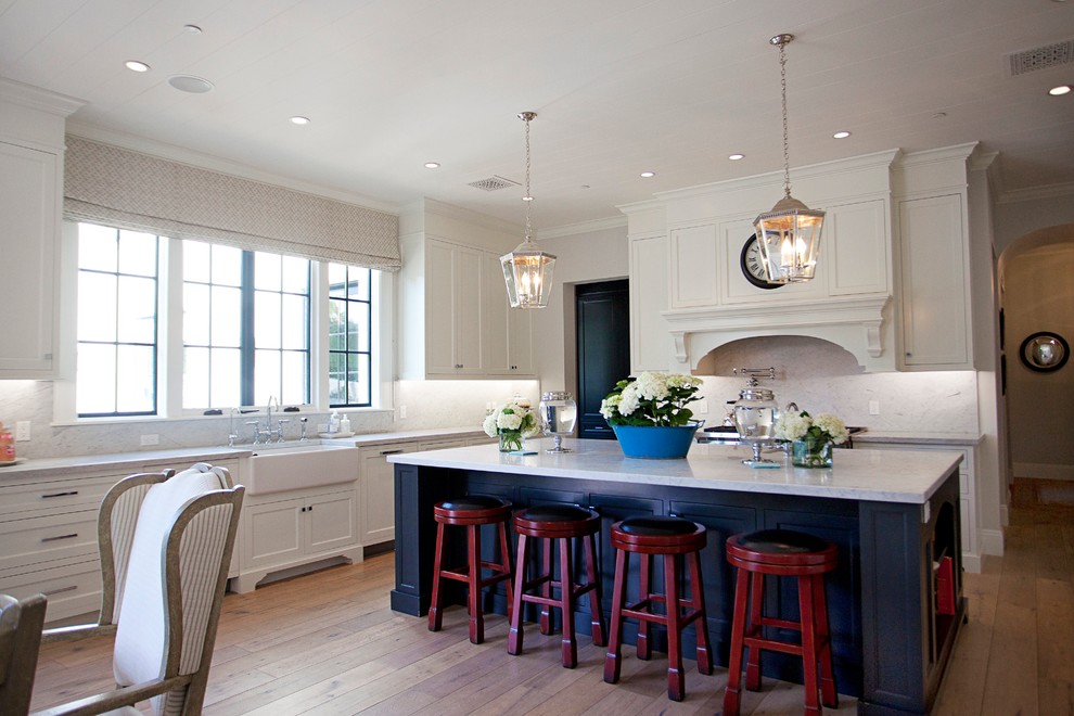 Example of a large farmhouse single-wall light wood floor and brown floor eat-in kitchen design in Phoenix with a farmhouse sink, recessed-panel cabinets, white cabinets, marble countertops, white backsplash, marble backsplash and an island