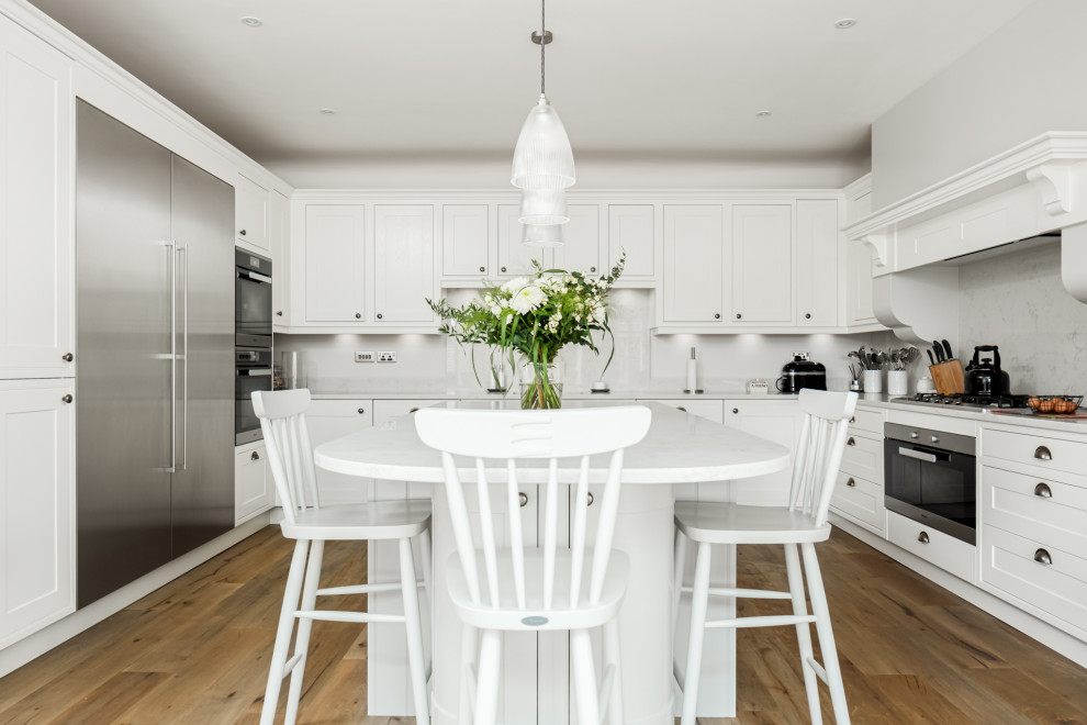 Klassische Küche mit Schrankfronten mit vertiefter Füllung, grauen Schränken, Marmor-Arbeitsplatte, Küchenrückwand in Weiß, Rückwand aus Marmor, braunem Holzboden, Kücheninsel und weißer Arbeitsplatte in Dorset