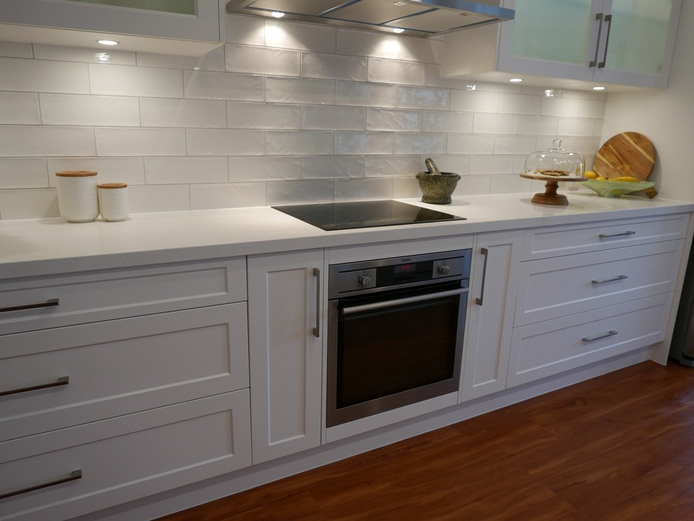 Example of a mid-sized beach style galley laminate floor kitchen pantry design in Brisbane with an undermount sink, shaker cabinets, white cabinets, quartz countertops, white backsplash, subway tile backsplash, stainless steel appliances and an island