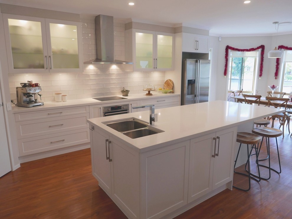 Example of a mid-sized beach style galley laminate floor kitchen pantry design in Brisbane with an undermount sink, shaker cabinets, white cabinets, quartz countertops, white backsplash, subway tile backsplash, stainless steel appliances and an island