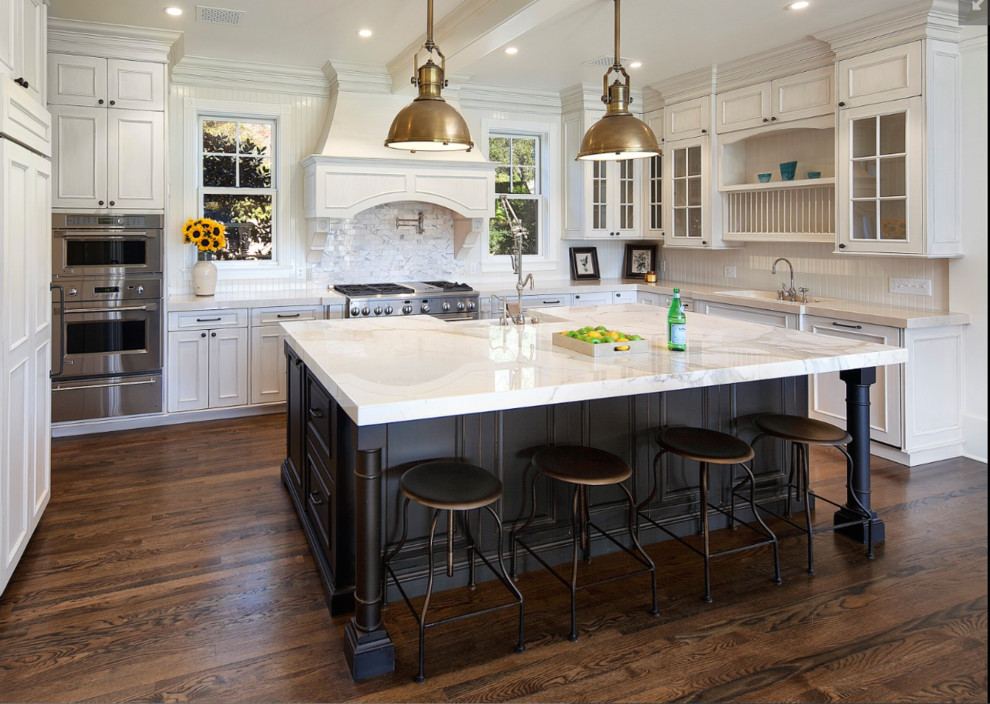Medium sized country l-shaped kitchen/diner in Santa Barbara with raised-panel cabinets, white cabinets, composite countertops, stainless steel appliances, dark hardwood flooring, an island, a belfast sink, beige splashback, wood splashback and brown floors.