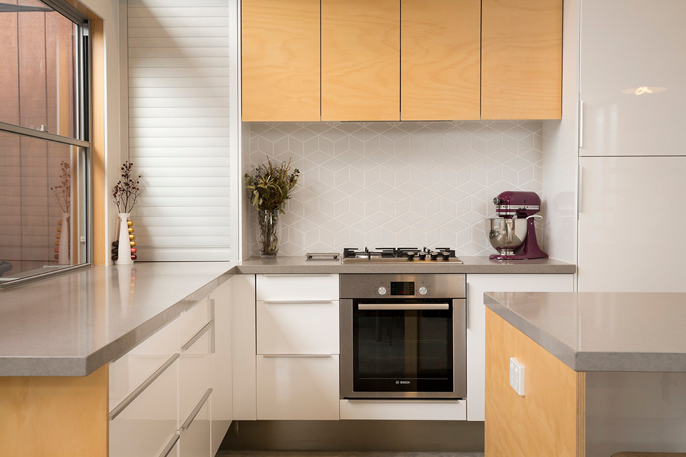 Bild på ett litet funkis kök, med skåp i ljust trä, bänkskiva i kvarts, grått stänkskydd, stänkskydd i keramik, rostfria vitvaror, betonggolv och en köksö