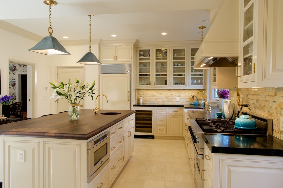 This is an example of a large classic l-shaped enclosed kitchen in Los Angeles with white cabinets, beige splashback, an island, raised-panel cabinets, wood worktops, ceramic splashback, integrated appliances, travertine flooring and a submerged sink.