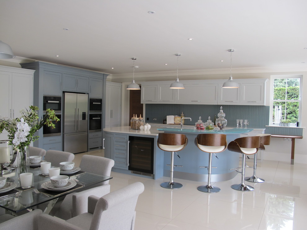 Große Moderne Wohnküche mit Schrankfronten mit vertiefter Füllung, weißen Schränken, Mineralwerkstoff-Arbeitsplatte, Küchenrückwand in Blau, Glasrückwand, Küchengeräten aus Edelstahl und Kücheninsel in Surrey
