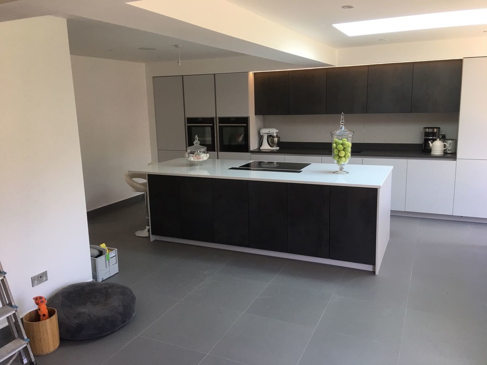 Design ideas for a contemporary single-wall open plan kitchen in London with a built-in sink, flat-panel cabinets, grey cabinets, quartz worktops, black appliances, porcelain flooring, an island and grey floors.