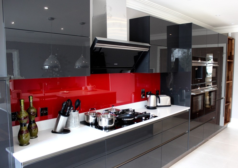 Photo of a large modern single-wall kitchen/diner in Buckinghamshire with a built-in sink, flat-panel cabinets, grey cabinets, quartz worktops, red splashback, glass sheet splashback, stainless steel appliances, porcelain flooring and an island.