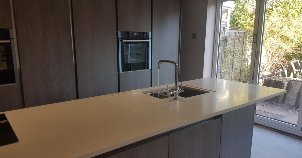 Moderne Wohnküche mit integriertem Waschbecken, flächenbündigen Schrankfronten, Mineralwerkstoff-Arbeitsplatte, Kücheninsel und weißer Arbeitsplatte in West Midlands
