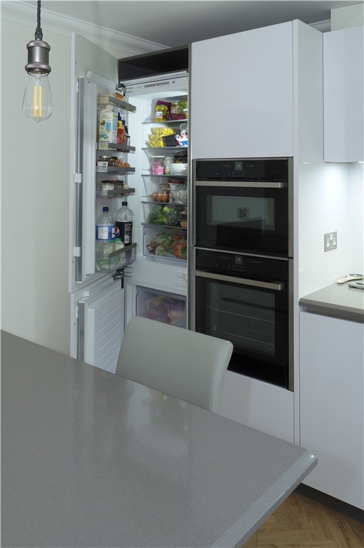 Modelo de cocina comedor moderna de tamaño medio con puertas de armario blancas, electrodomésticos negros, península, suelo marrón y encimeras grises