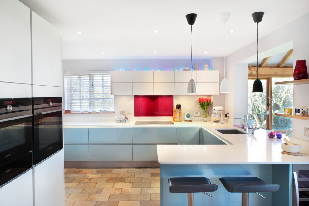 バッキンガムシャーにある中くらいなコンテンポラリースタイルのおしゃれなキッチン (フラットパネル扉のキャビネット、青いキャビネット、赤いキッチンパネル、ガラスタイルのキッチンパネル、シルバーの調理設備) の写真
