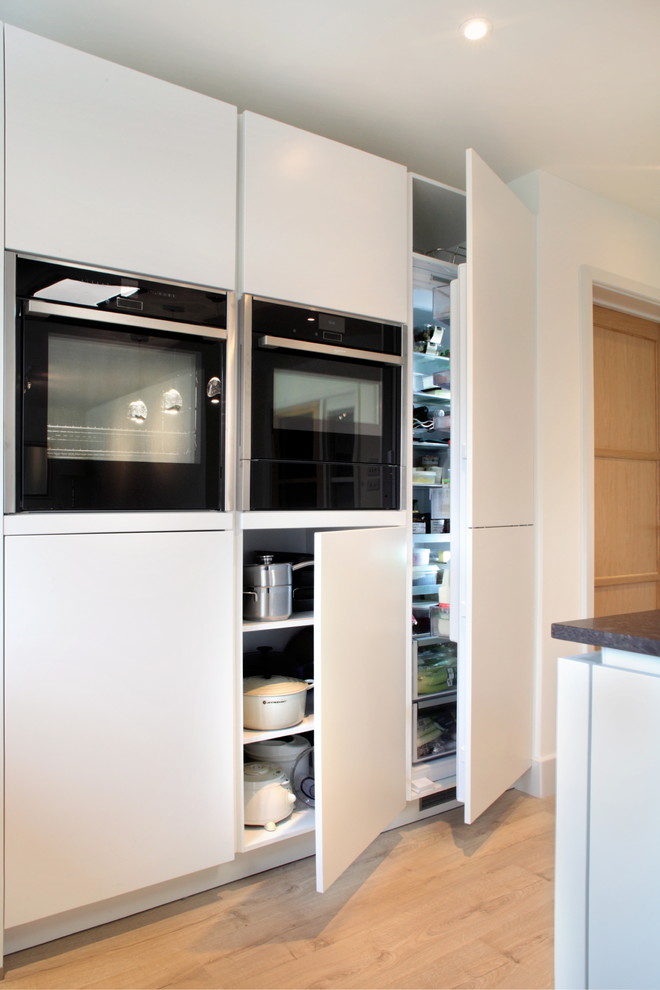 Foto på ett mellanstort funkis kök, med släta luckor, vita skåp, bänkskiva i kvartsit, mellanmörkt trägolv, en köksö, en integrerad diskho och svarta vitvaror