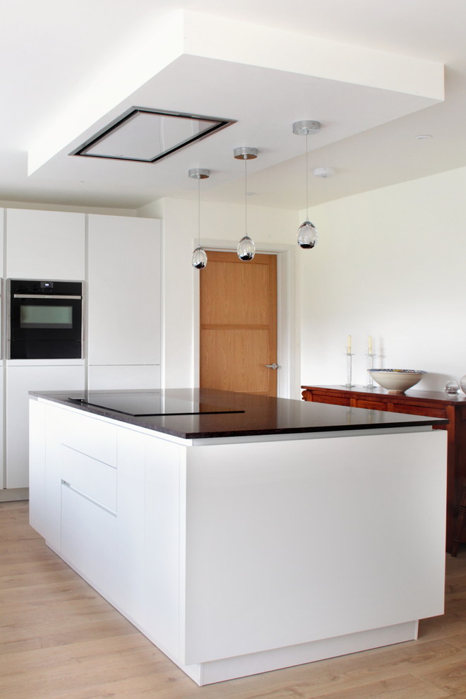 Foto di una cucina minimal di medie dimensioni con ante lisce, ante bianche, top in quarzite, pavimento in legno massello medio, lavello integrato e elettrodomestici neri