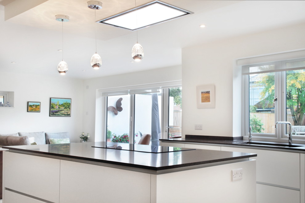 Medium sized contemporary l-shaped kitchen/diner in Buckinghamshire with flat-panel cabinets, white cabinets, quartz worktops, medium hardwood flooring, an island, an integrated sink and black appliances.