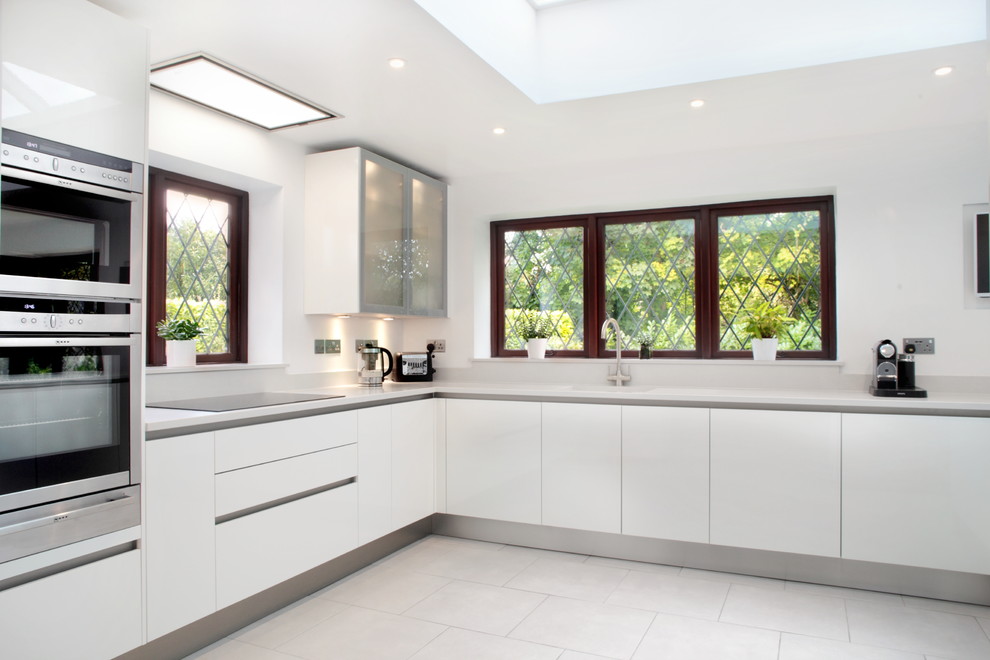 This is an example of a large contemporary u-shaped kitchen/diner in Buckinghamshire with flat-panel cabinets, white cabinets, quartz worktops, stainless steel appliances, a breakfast bar, a submerged sink and porcelain flooring.