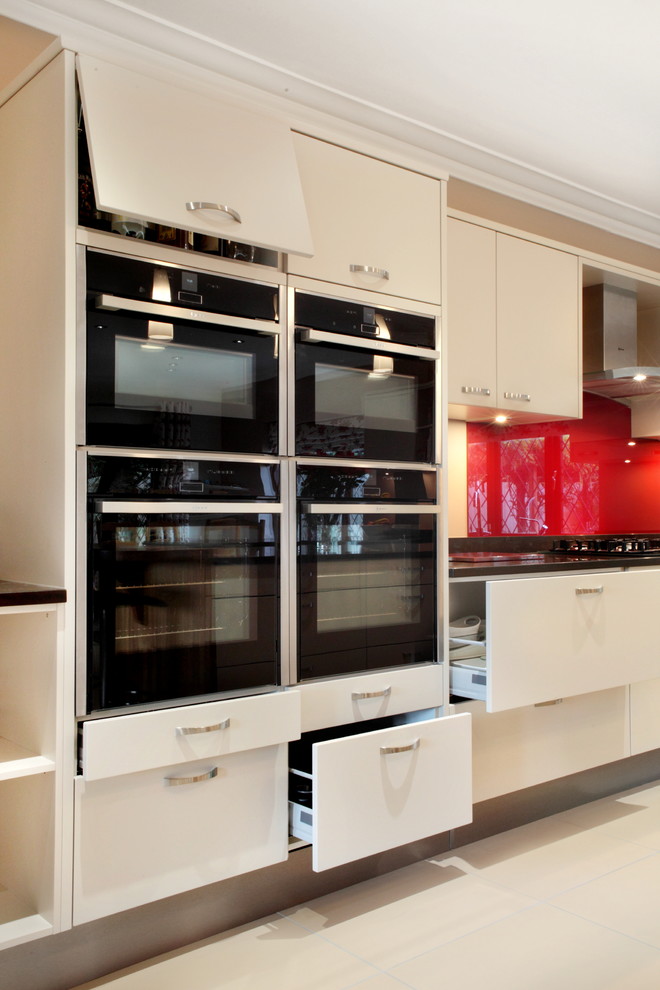 Design ideas for a large contemporary u-shaped kitchen/diner in Buckinghamshire with flat-panel cabinets, beige cabinets, quartz worktops, red splashback, glass sheet splashback, porcelain flooring, an island, a submerged sink and stainless steel appliances.