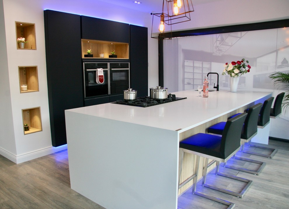 This is an example of a large contemporary single-wall open plan kitchen in London with a built-in sink, flat-panel cabinets, blue cabinets, quartz worktops, integrated appliances, laminate floors, an island and white worktops.