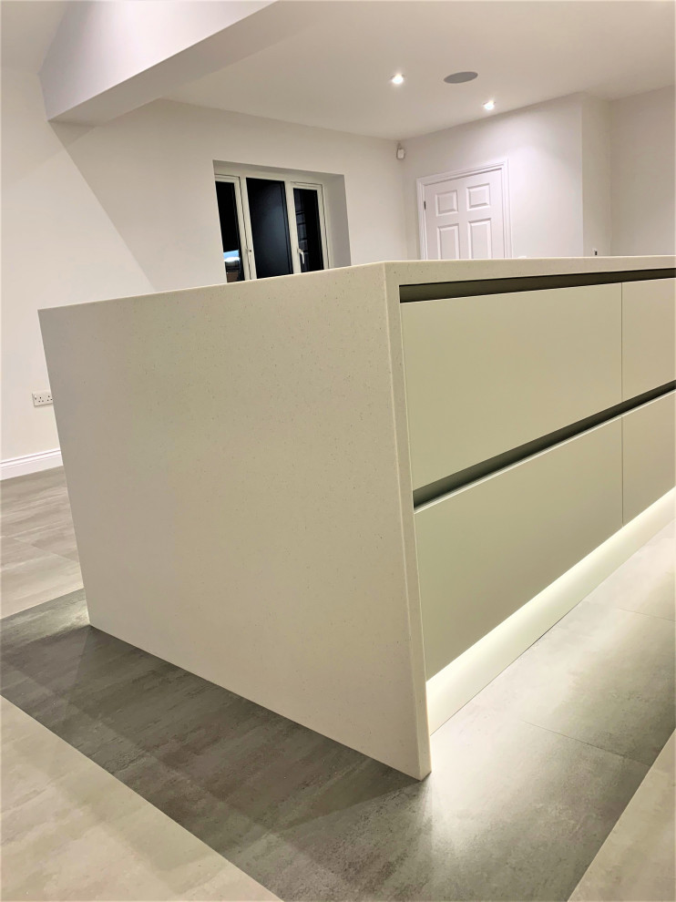 Large contemporary single-wall open plan kitchen in Other with an integrated sink, flat-panel cabinets, medium wood cabinets, composite countertops, black appliances, vinyl flooring, an island and white worktops.